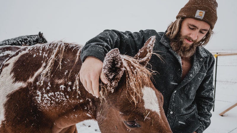man kneeled down petting pony